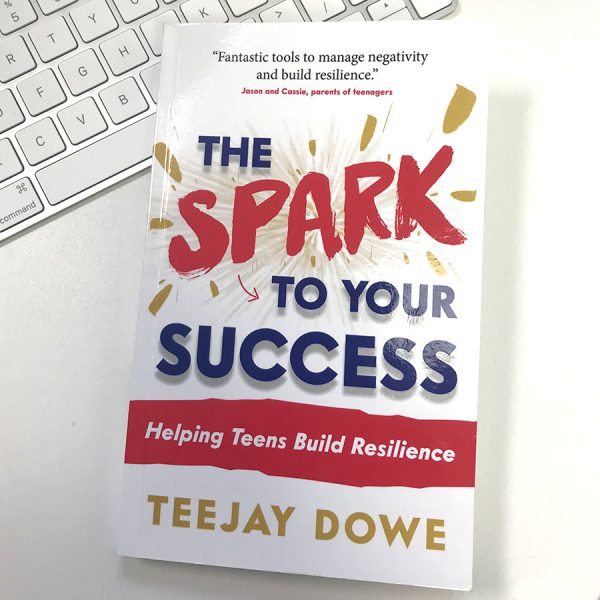 The Spark to Your Success book by TeeJay Dowe resting on a desk next to a keyboard